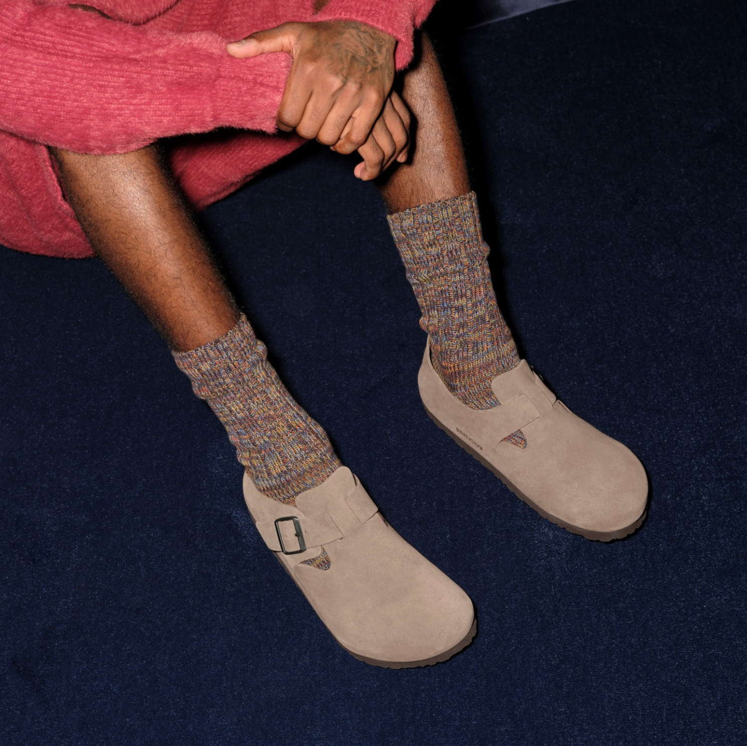 Person wearing brown socks and beige birkenstock shoes on a dark blue background