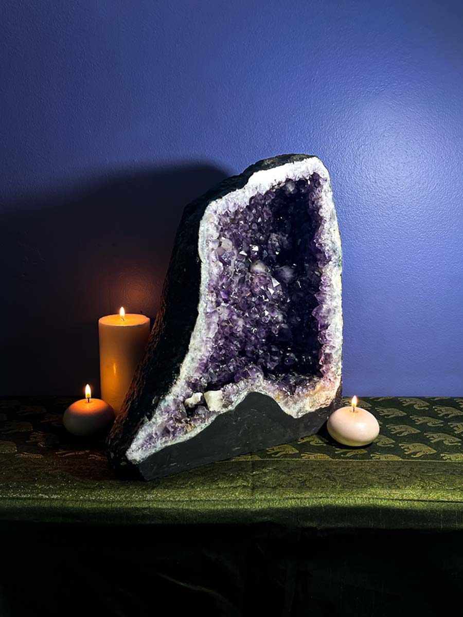 Amethyst geode with candles on a dark surface against a blue wall