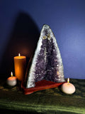 Amethyst crystal pyramid with candles on a dark surface against a blue wall