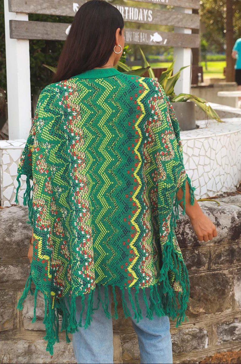 Person wearing a green patterned shawl with fringes, standing outdoors.
