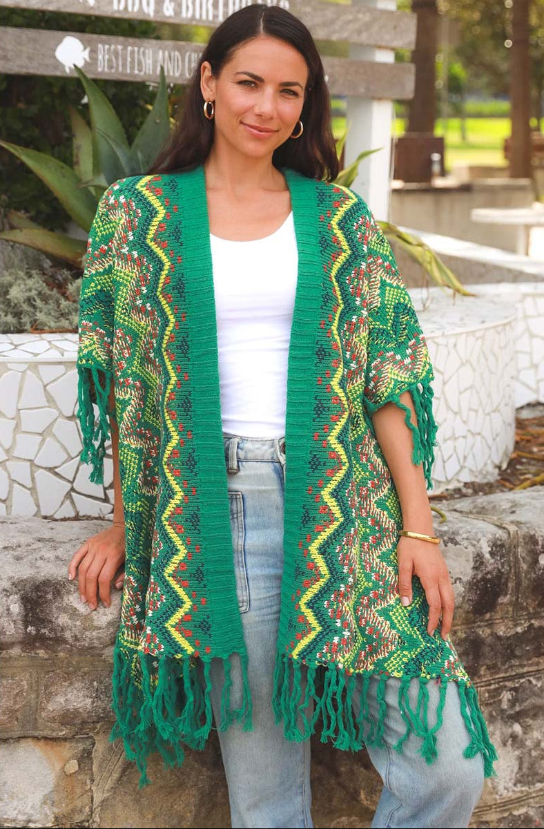 Woman wearing a green patterned cardigan with fringe in an outdoor setting.
