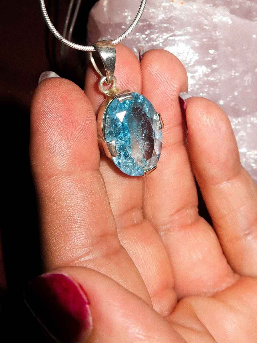Blue gemstone pendant on a silver chain held in a hand.