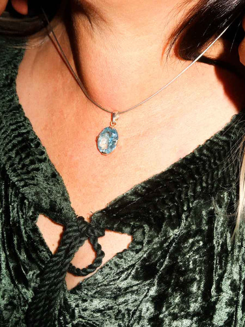 Close-up of a person wearing a green velvet top with a necklace featuring a blue gemstone pendant.