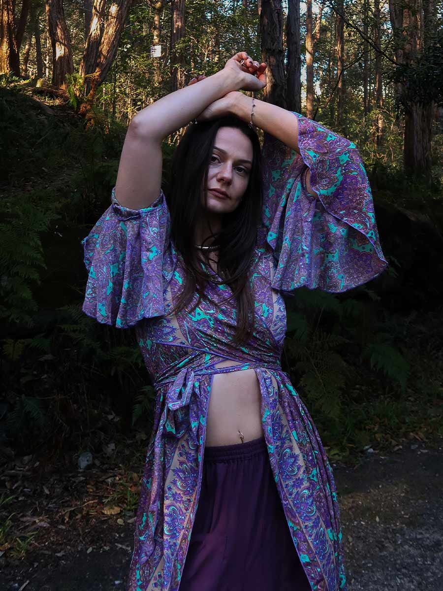 Woman in a purple patterned outfit standing in a forest