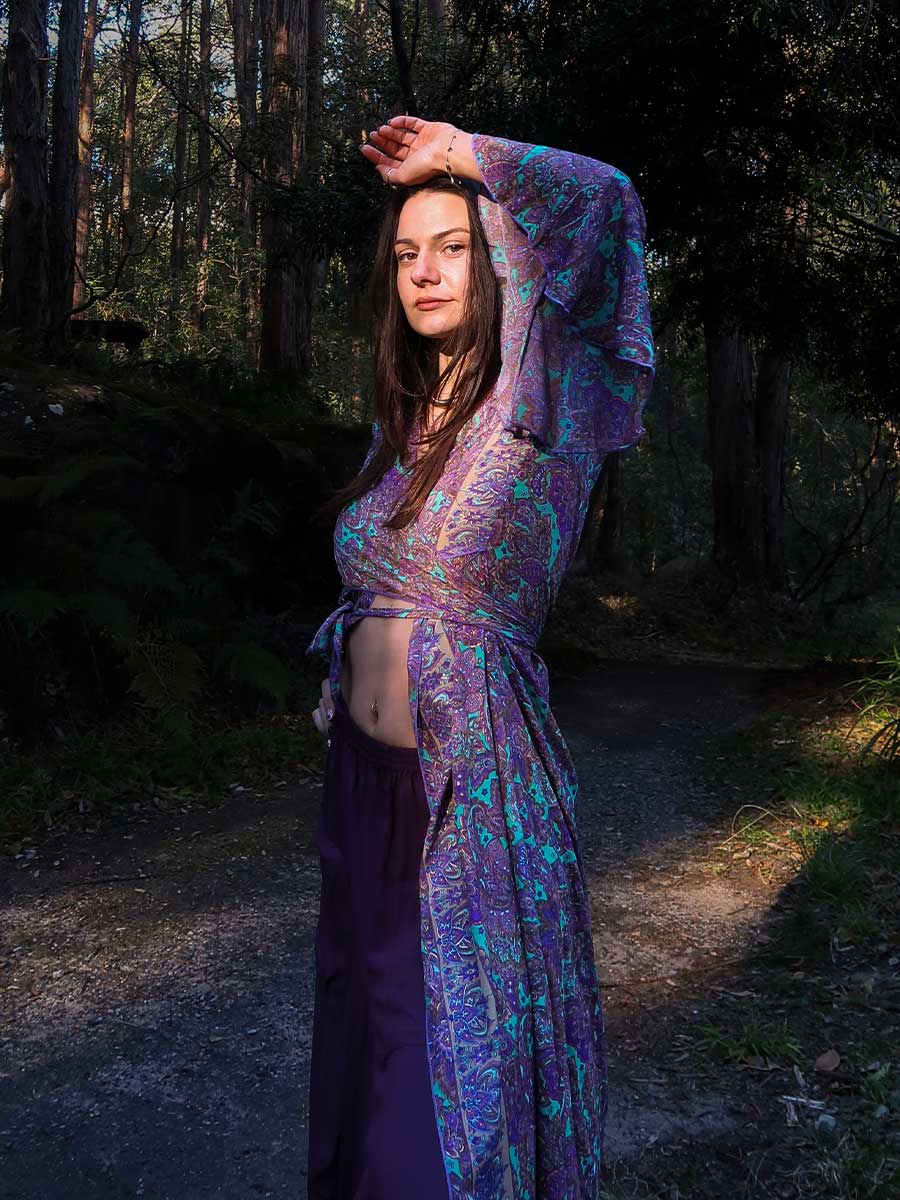 Woman in a purple and blue patterned outfit standing in a forest