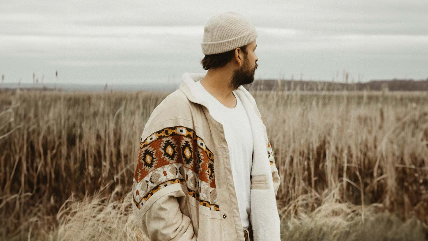 Man wearing a patterned jacket and beanie standing in a field