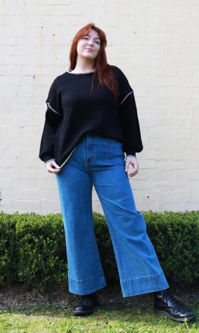 A woman wearing blue, flared jeans and a black sweater.