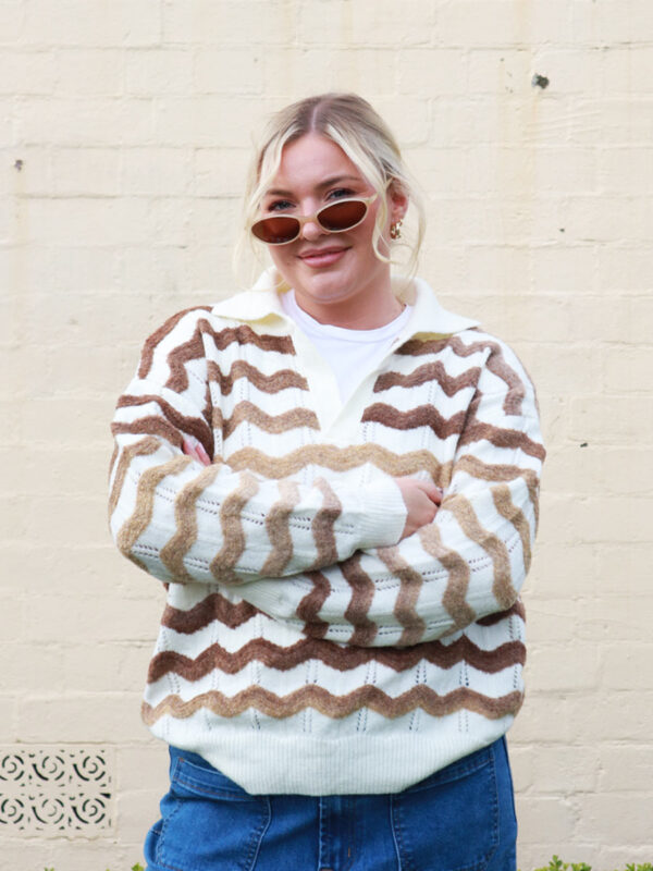 A woman wearing a polo neck, cream knit with earthy-toned zig-zag details.