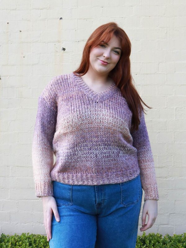 A woman wearing an earthy-toned, multi-coloured, v-neck, knit sweater.