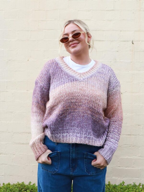 A woman wearing an earthy-toned, multi-coloured, v-neck, knit sweater.