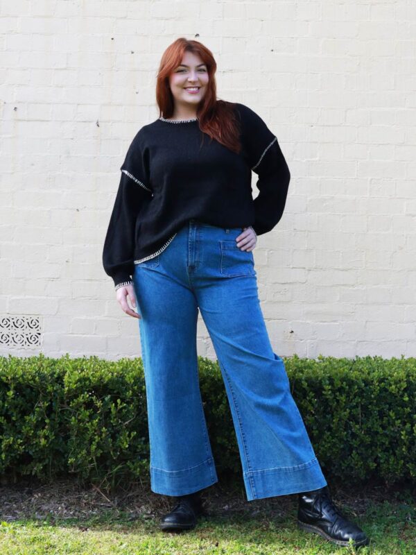 A woman wearing a black knit sweater with white contrast stitching on the cuffs and hems.