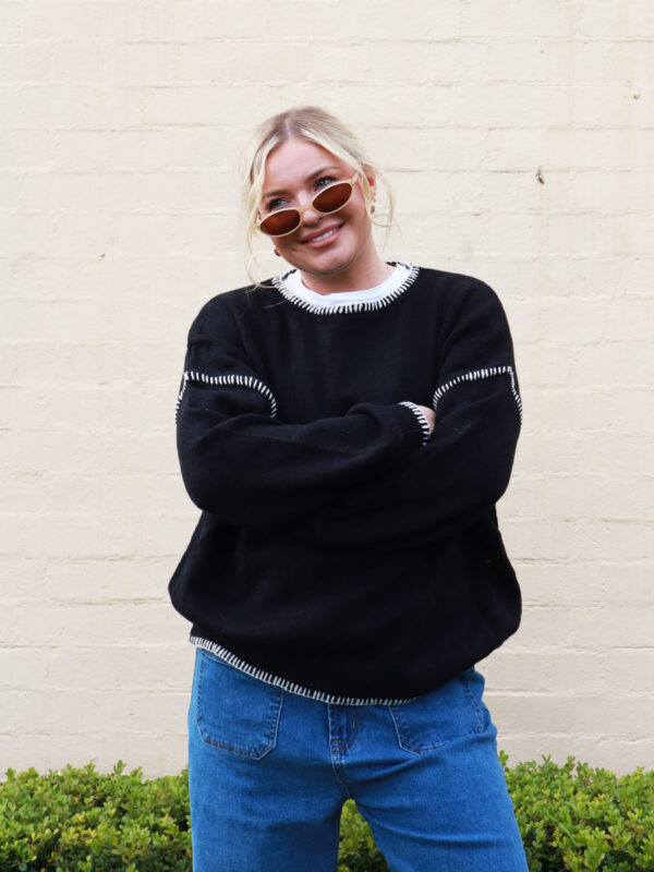 A woman wearing a black knit sweater with white contrast stitching on the cuffs and hems.