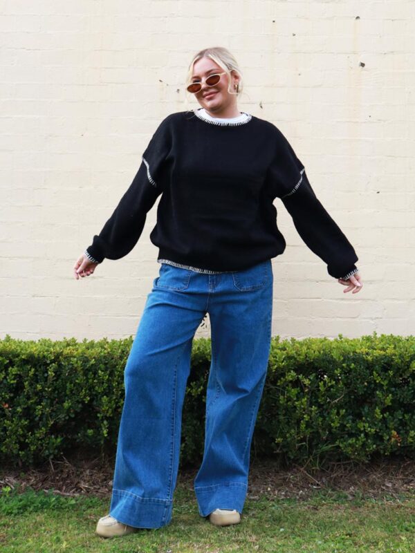 A woman wearing a black knit sweater with white contrast stitching on the cuffs and hems.