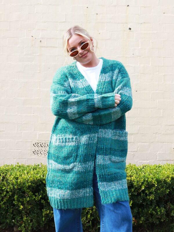 A woman wearing a knitted, green-striped, long, cardigan.