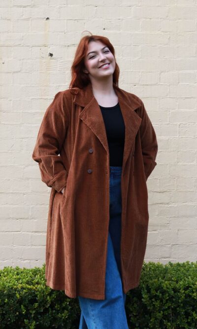 A tall woman wearing a chocolate brown, knee length corduroy coat.