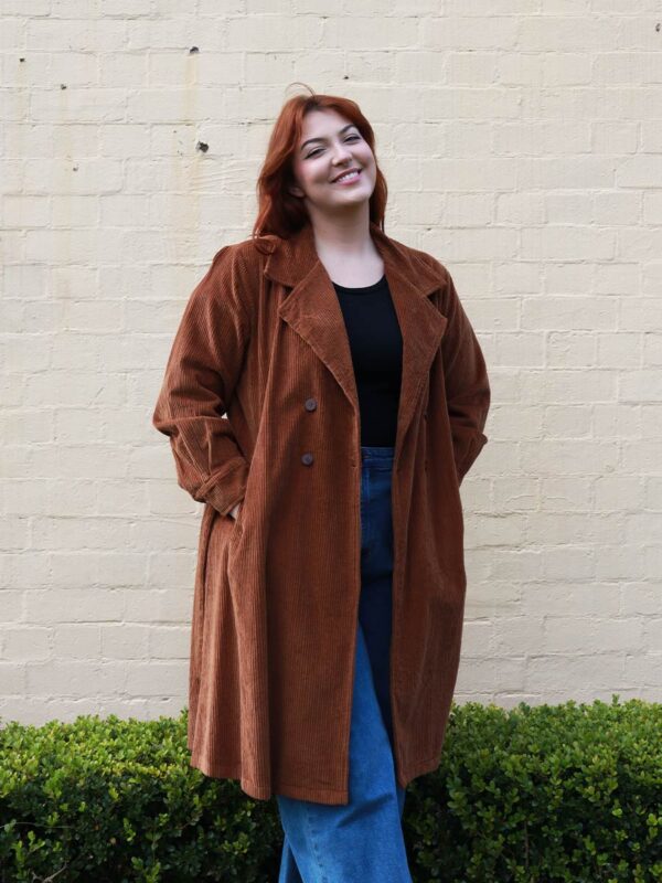 A tall woman wearing a chocolate brown, knee length corduroy coat.