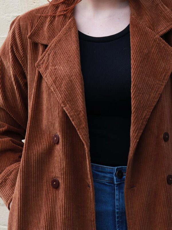 A tall woman wearing a chocolate brown, knee length corduroy coat.