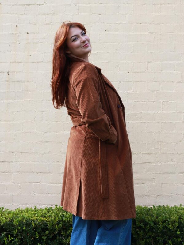 A tall woman wearing a chocolate brown, knee length corduroy coat.