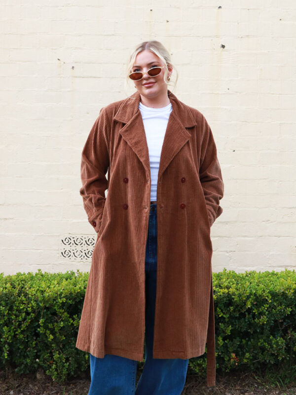 A woman wearing a chocolate brown, knee length corduroy coat.