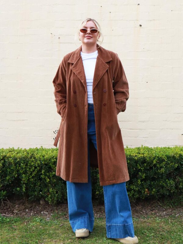 A woman wearing a chocolate brown, knee length corduroy coat.