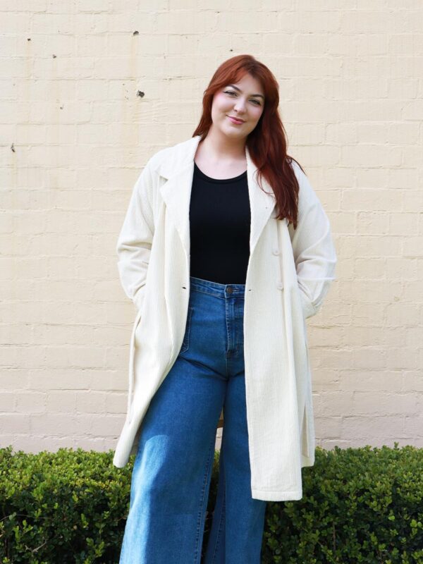 A tall woman wearing a taupe, knee-length corduroy coat.