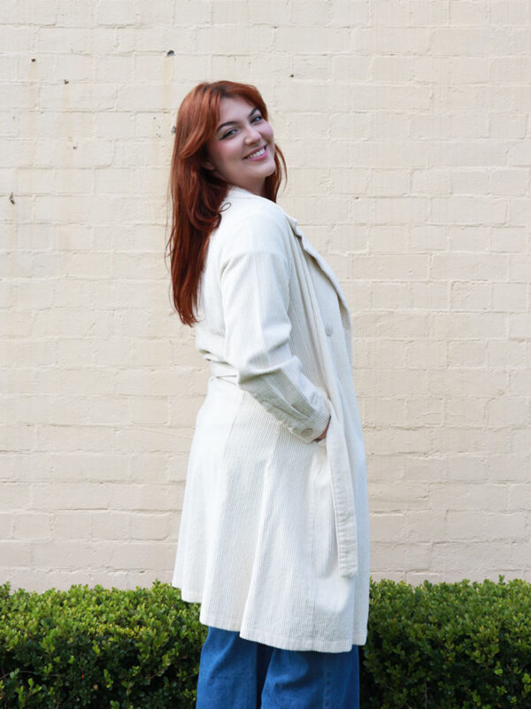 A tall woman wearing a taupe, knee-length corduroy coat.