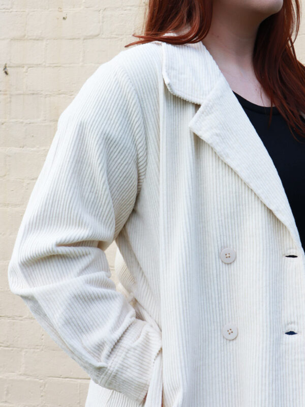 A tall woman wearing a taupe, knee-length corduroy coat.