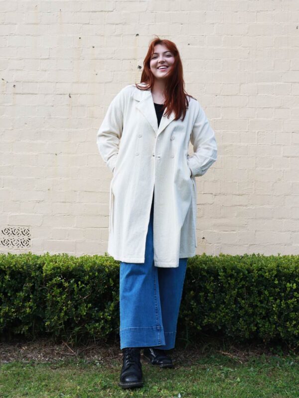 A tall woman wearing a taupe, knee-length corduroy coat.