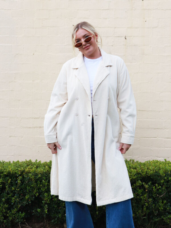 A woman wearing a taupe, knee-length corduroy coat.