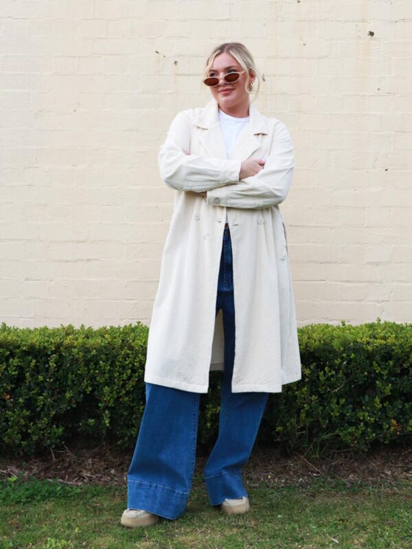 A woman wearing a taupe, knee-length corduroy coat.