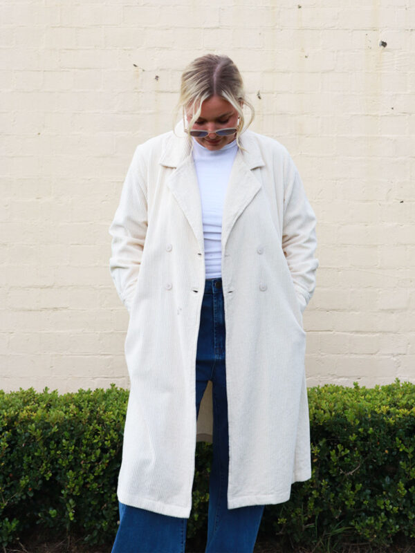 A woman wearing a taupe, knee-length corduroy coat.