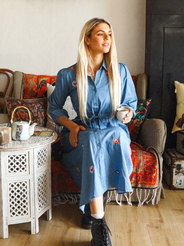 woman sitting on a couch drinking tea wearing a blue denim maxi dress