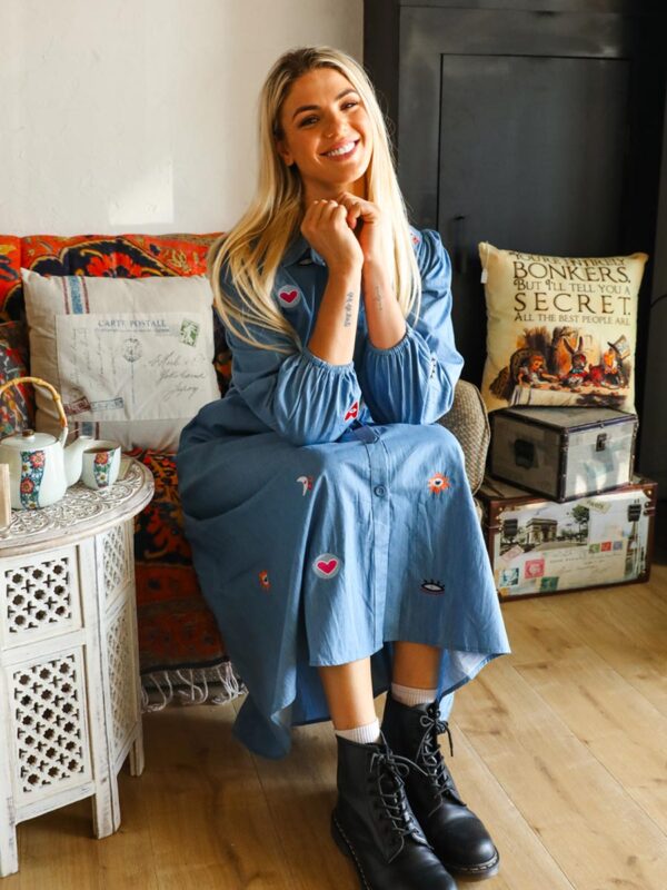 woman sitting on a couch drinking tea wearing a blue denim maxi dress